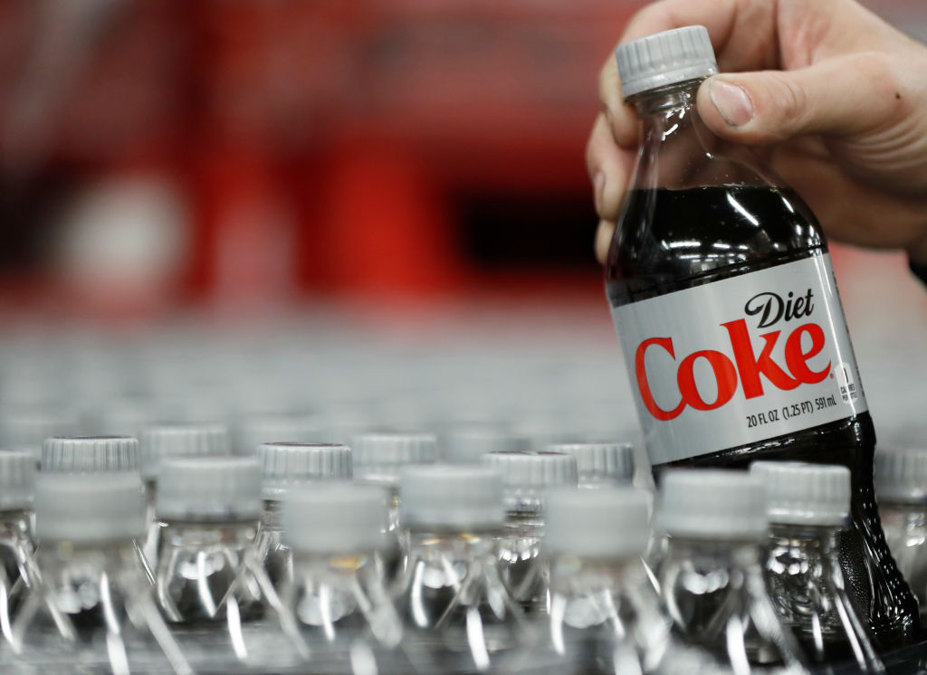 A Diet Coke bottle being pulled from a pile of other bottles.